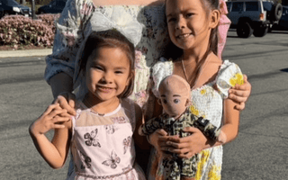 Three young girls in floral dresses holding a doll, promoting empathy through play and storytelling.
