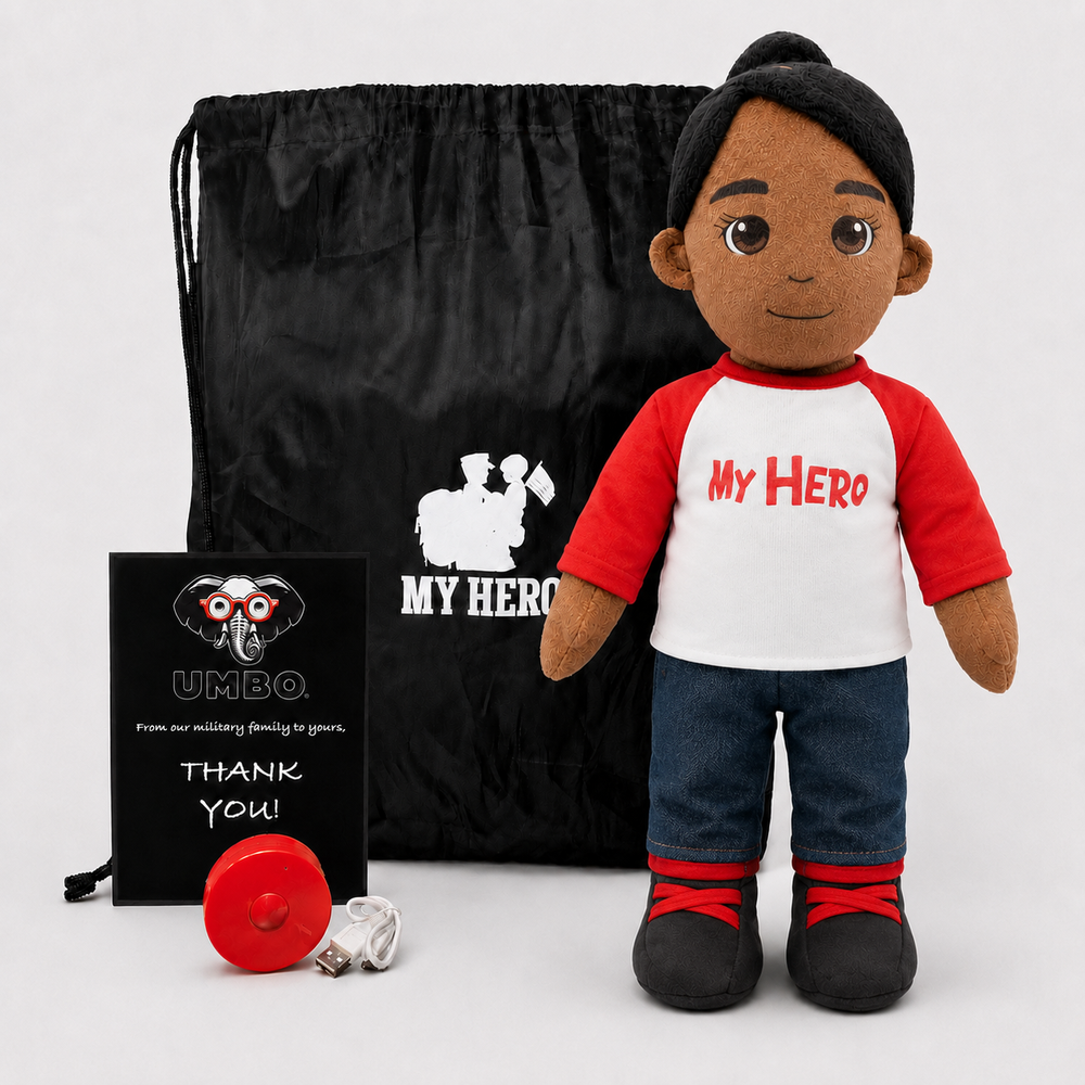 A plush doll with dark skin, black hair, a red-and-white shirt reading 'My Hero,' blue jeans, and black shoes stands in front of a black drawstring bag and a small black card on a light gray background.