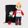 A plush doll with blond hair, a red and white shirt reading 'MY HERO', blue jeans, and red-and-gray shoes stands beside a black drawstring bag with a white 'MY HERO' logo and a small red accessory on a light gray background.