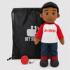 A plush doll toy stands in front of a black drawstring bag with a white 'MY HERO' graphic. The doll wears a black cap, a red-and-white raglan shirt with 'My Hero' in red text, blue jeans, and black shoes with red laces.