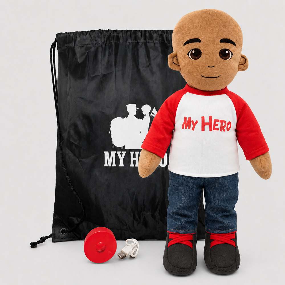 A plush doll toy with a bald head and brown skin, wearing a red and white raglan shirt that says 'MY HERO' in red, blue jeans, and black-and-red shoes, shown with a black drawstring bag and a red circular accessory on a light gray background.