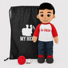 A plush doll with a 'My Hero' theme stands next to a black drawstring bag with a white graphic and text, with a red cap and a small white accessory on a light gray background.