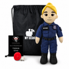Police Officer Plush doll stands in front of a black drawstring bag and a small black gift card. The doll has a yellow helmet/hair, a beige face and arms, and is dressed in a blue uniform with black boots.