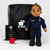 A custom plush toy police officer doll with a navy blue uniform, black boots, and a brown skin tone, displayed alongside a black drawstring bag, a black thank-you card, and a small red accessory on a light gray background.
