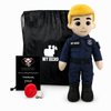 A plush toy dressed as a police officer stands in front of a black drawstring bag, with a small black card and a red round accessory on a white studio background. The plush has a yellow hair/hood, beige skin, and a navy uniform with 'MY HERO' text and patches.