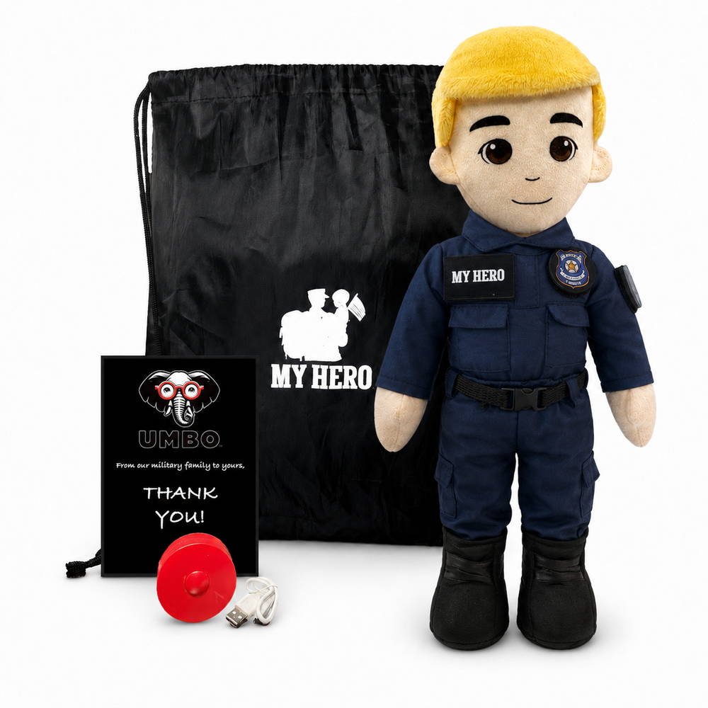A plush toy dressed as a police officer stands in front of a black drawstring bag, with a small black card and a red round accessory on a white studio background. The plush has a yellow hair/hood, beige skin, and a navy uniform with 'MY HERO' text and patches.