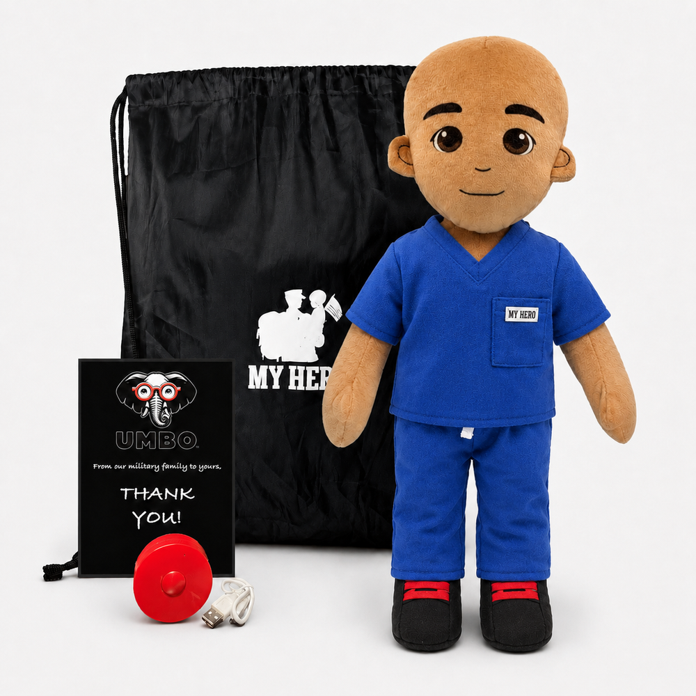 A plush military-themed doll dressed in blue medical scrubs stands in front of a black drawstring bag and a black plaque. The doll has a bald head, brown skin, and black shoes with red accents.