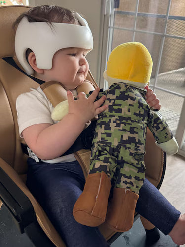 Child in a car seat holding a daddy doll with camouflage pattern