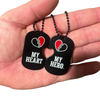 Two black heart-shaped dog tags on a bead chain with a white-and-red broken-heart emblem.